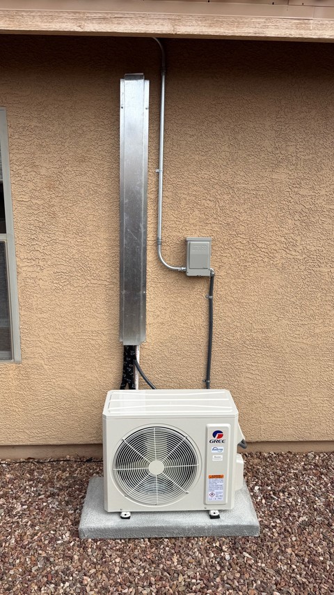 Outdoor mini-split on an equipment pad beside a stucco wall with a metal line cover