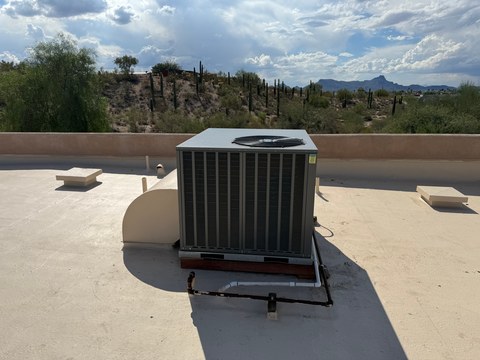 Rooftop packaged HVAC unit with connected ductwork and piping on a light-colored flat roof