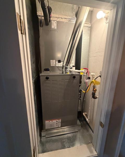 Furnace and indoor coil inside a narrow utility closet with metal vent pipe and condensate piping