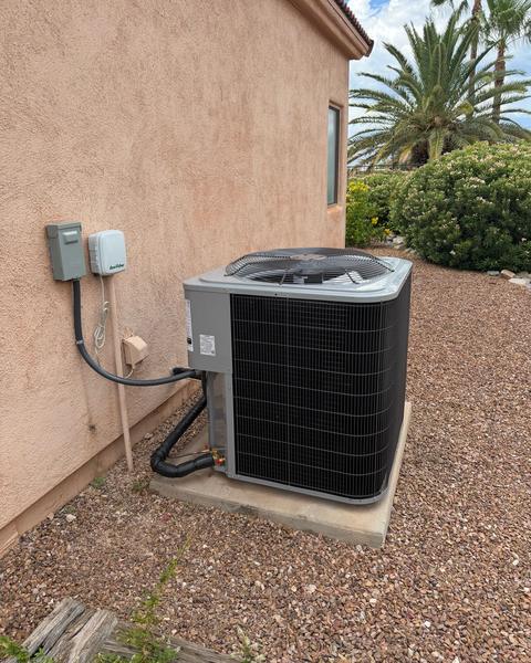 Outdoor condenser on a concrete pad beside a stucco wall, with insulated refrigerant lines and electrical disconnect