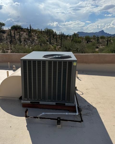 Packaged HVAC unit on a light-colored flat roof with piping run across the roof and desert hills behind